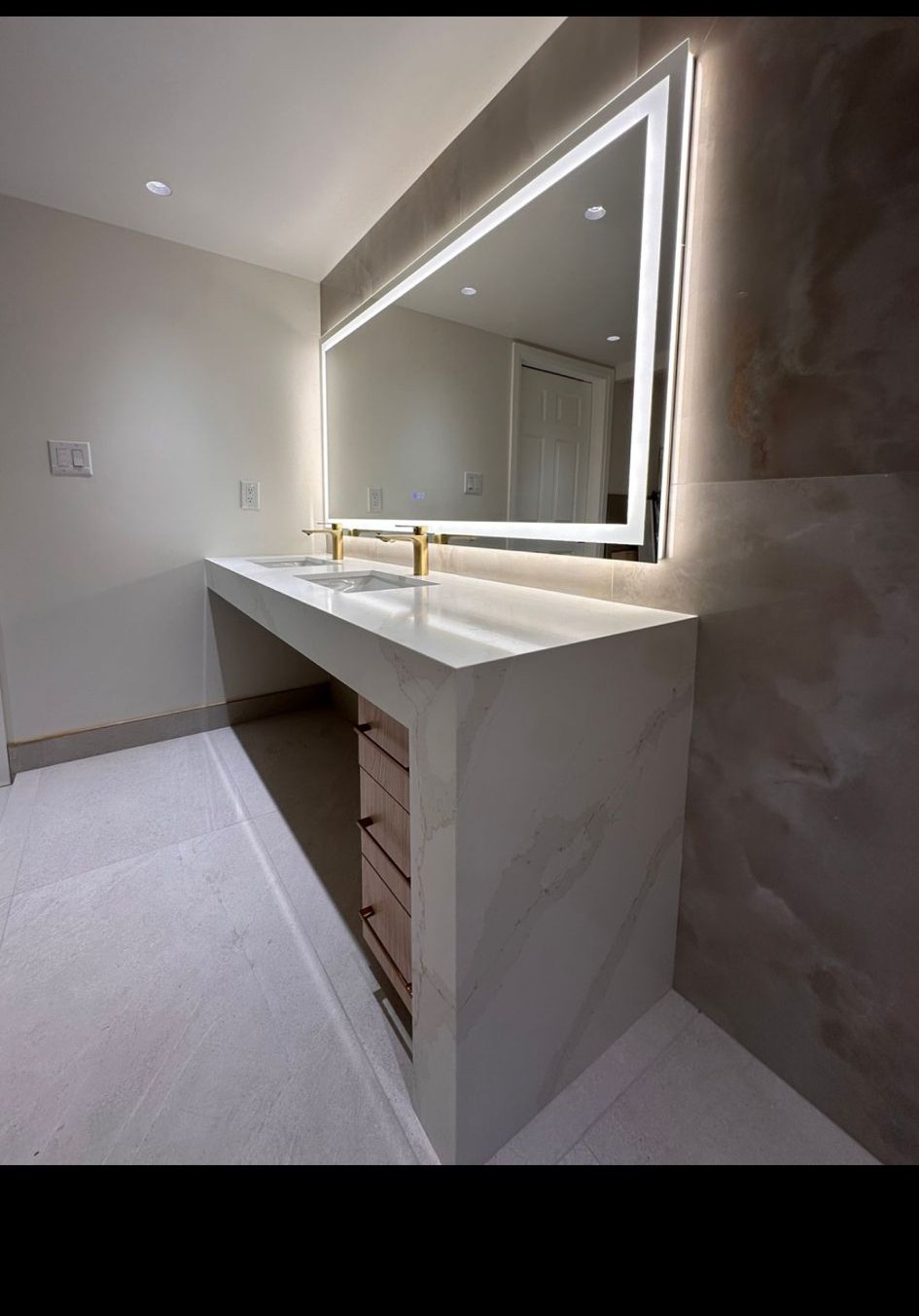 Floating roll-under quartz vanity with a backlit LED mirror and curbless tiled floor for wheelchair access