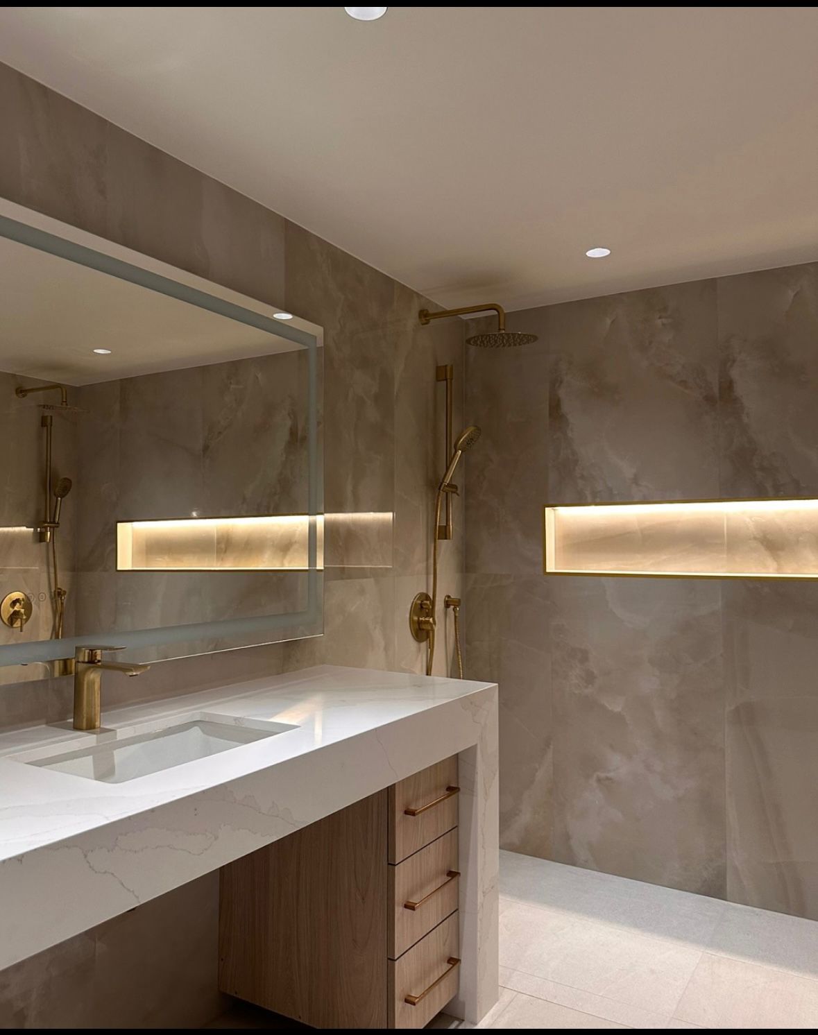 Modern curbless wet room with a floating quartz vanity, gold fixtures and a backlit feature niche