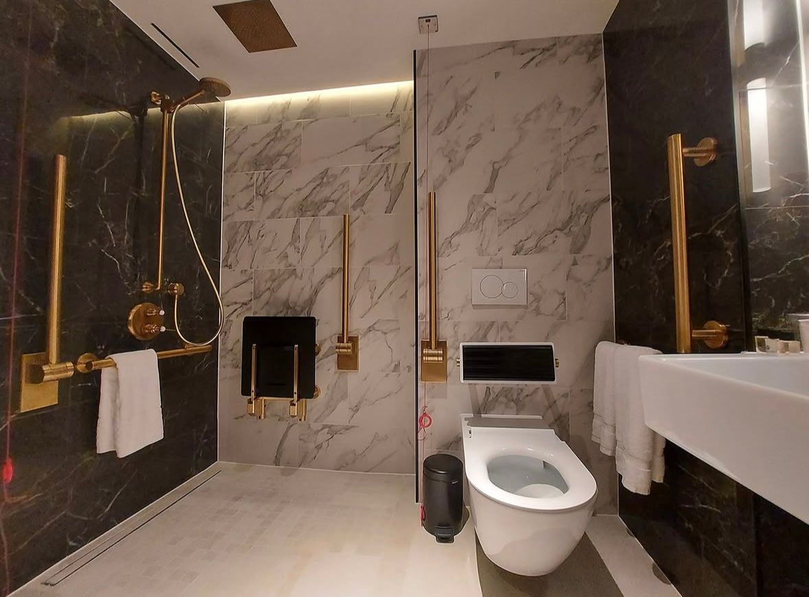Finished accessible curbless wet room in Metro Vancouver with gold grab bars, a fold-down shower seat and marble walls